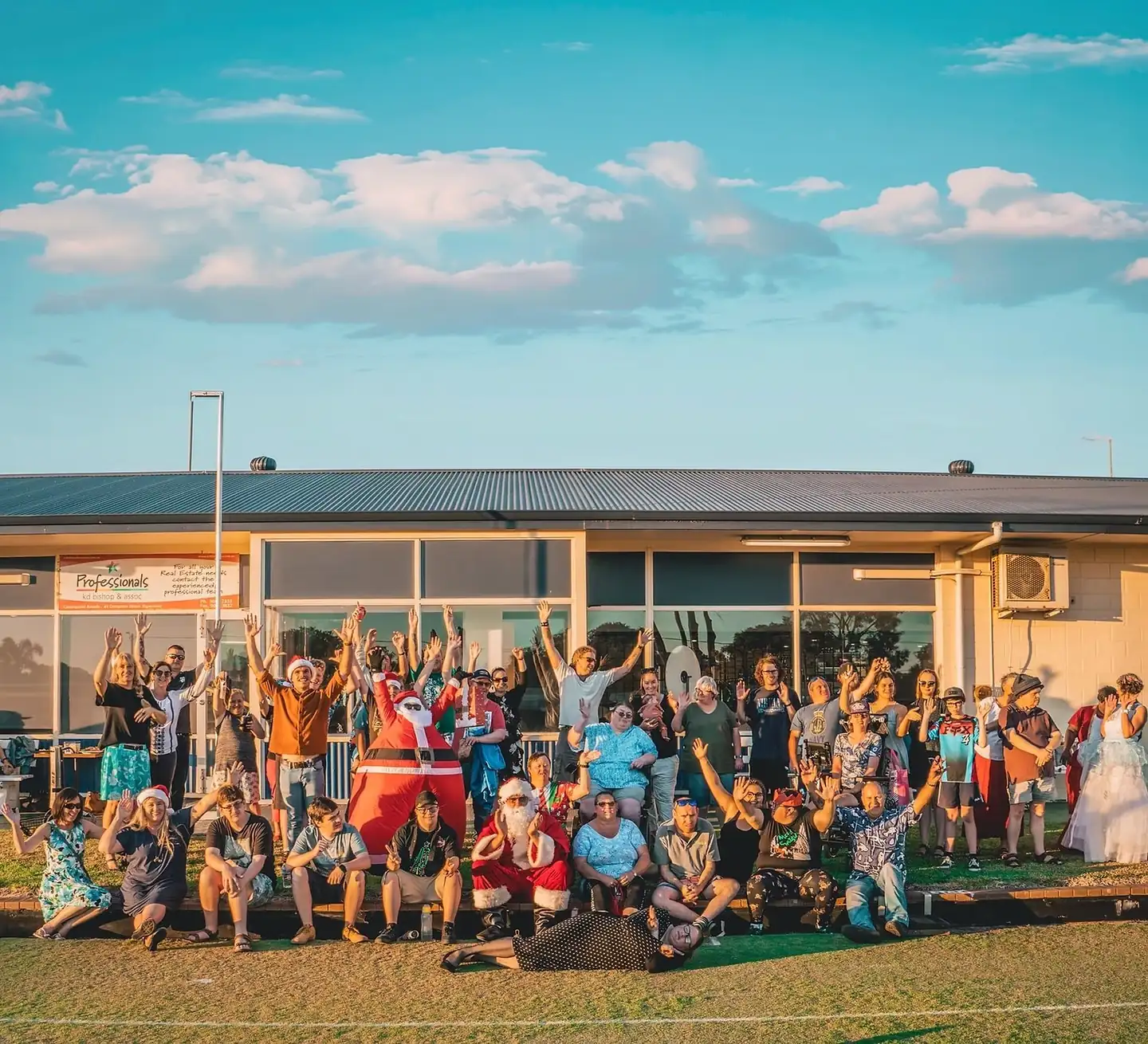 A large group of GIFSA participants, families and staff gathered outside for a community celebration, arms raised
